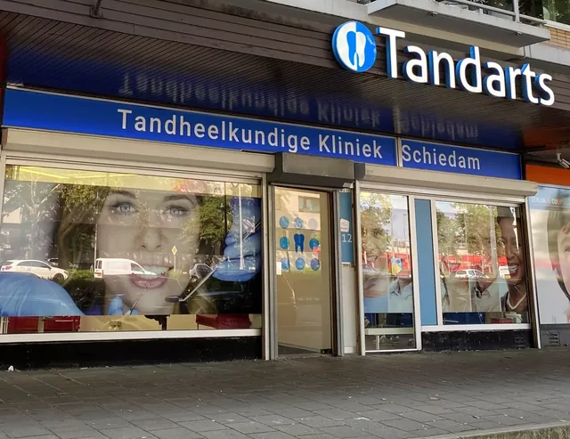 De voorkant van de praktijk aan de 's-Gravelandseweg 612: blauw bord Tandheelkundige Kliniek Schiedam, het Tandarts-logo en de glazen deur