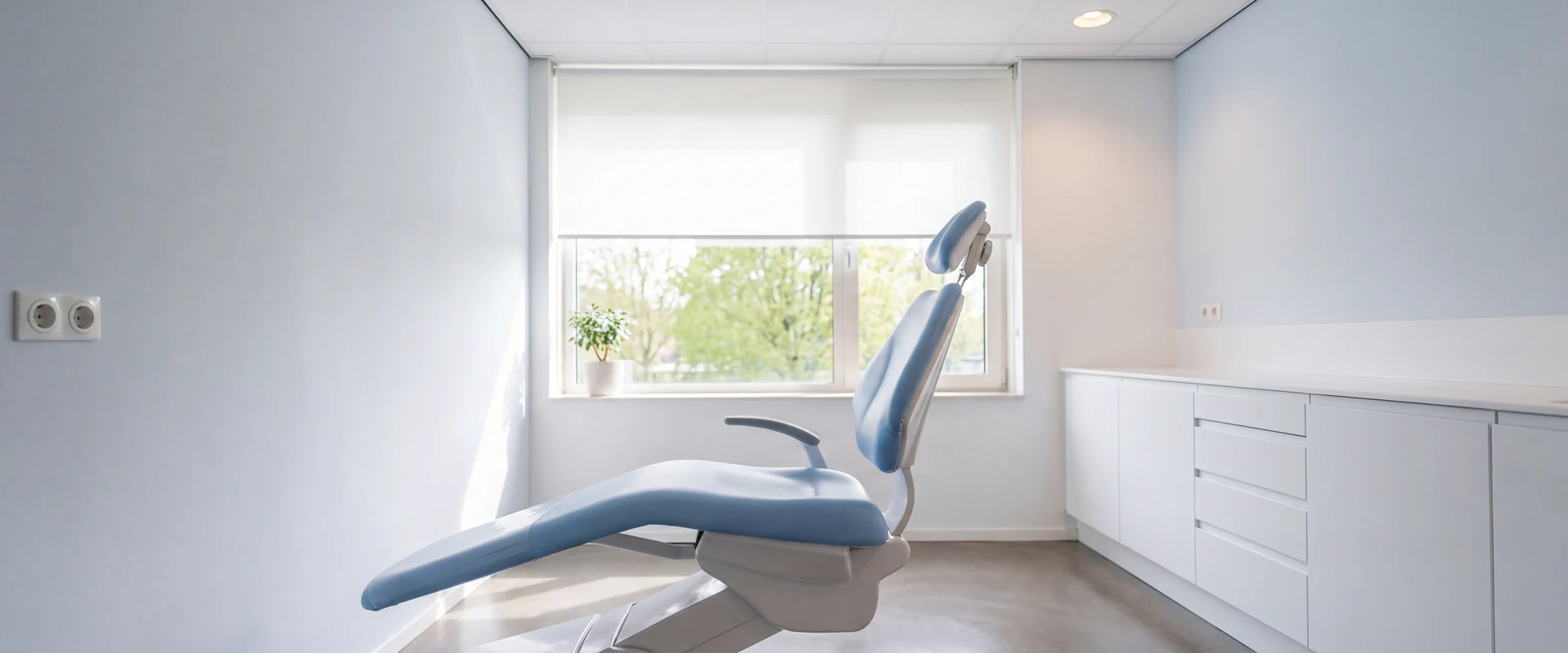 Lichte behandelkamer met een tandartsstoel en een groot raam