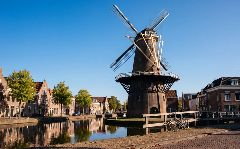 Molen aan een gracht met oude huizen onder een blauwe lucht