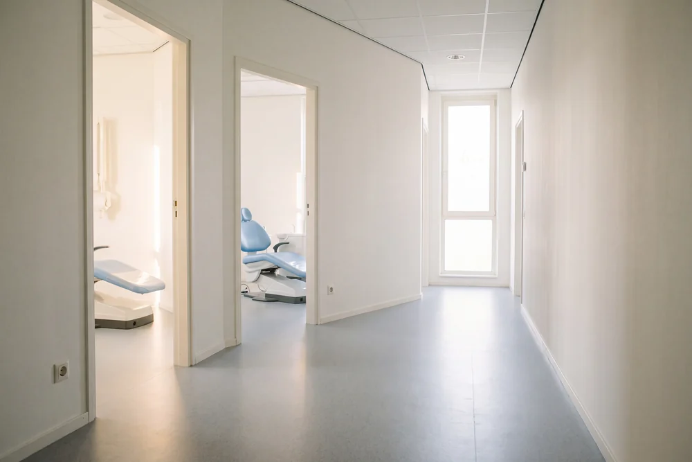 Lichte gang met open deuren naar behandelkamers met een blauwe behandelstoel